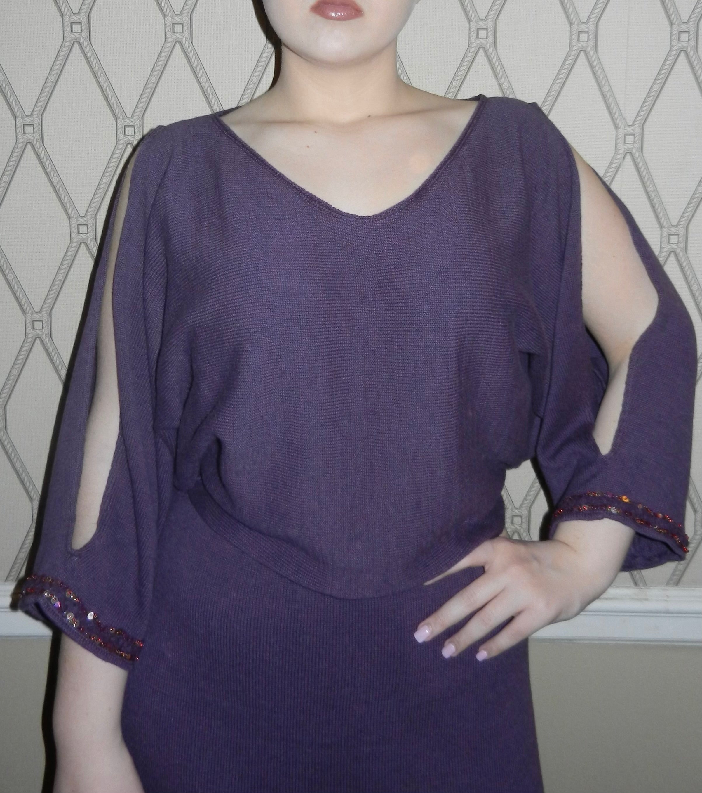 Woman wearing mulberry color 2-piece knit dress with long open sleeves with sequins beaded on sleeve opening. Soft wide v-neck pullover kimono sleeve sweater over a straight pull on knee length skirt in matching fabric. Photograph taken in a hallway.