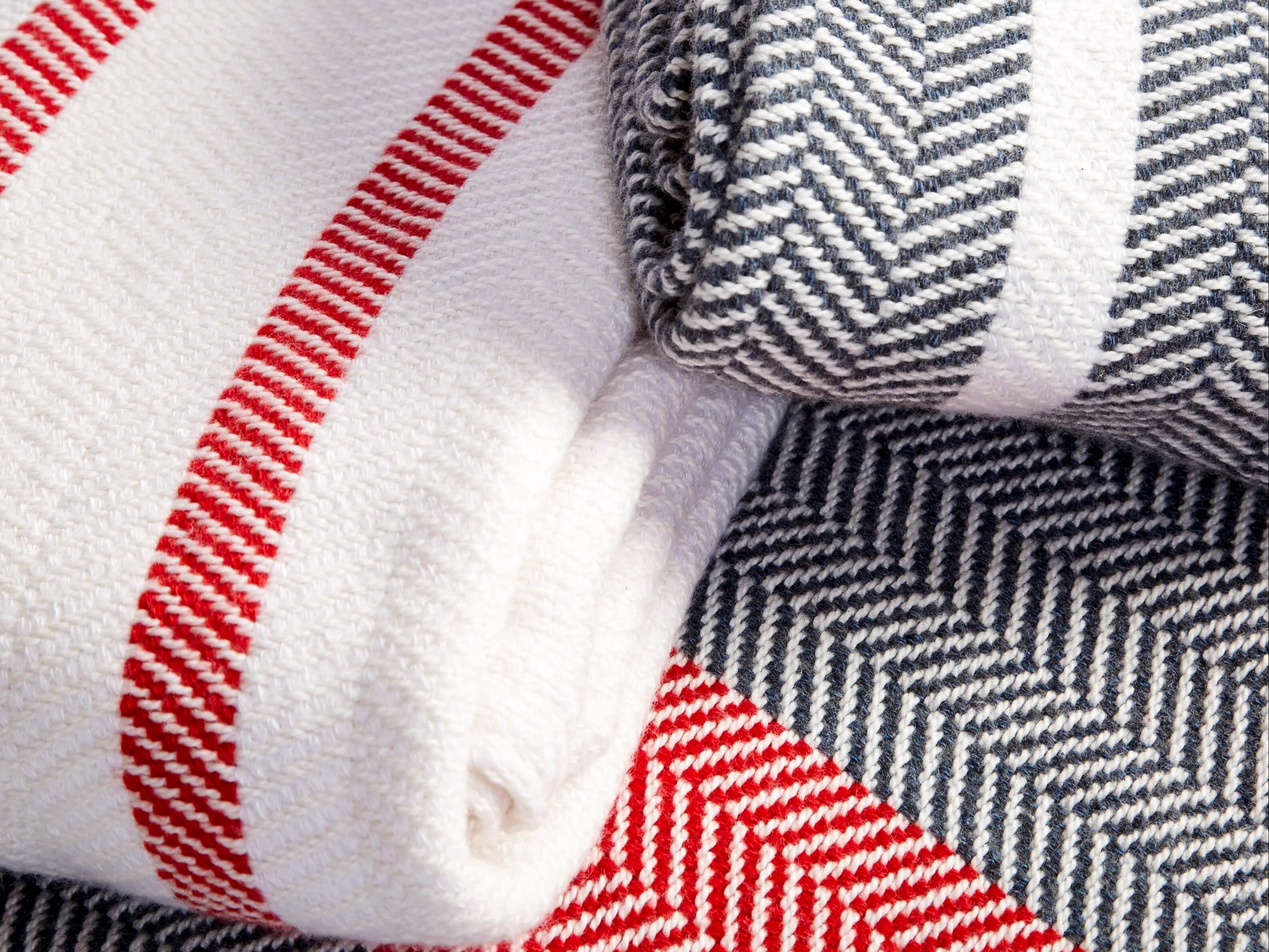 Close up photo of Vivloe Parlour Throw blankets in cotton and cashmere herringbone stripes in white and red, black and red, and grey and white